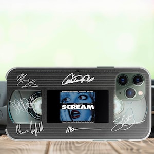 Puede incluir: Una funda para teléfono negra y transparente con un diseño de cinta VHS. La funda presenta una pantalla que muestra la película "Scream" y firmas del reparto. El texto "Inserte este lado en la grabadora. No toque el lado de la cinta." está impreso en la funda.