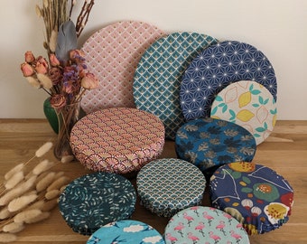 May include: A collection of ten round fabric bowl covers in various sizes, featuring diverse patterns including pink triangles, blue geometric shapes, yellow lemons, dark leaf prints, teal swallows, and pink flamingos on light blue fabric.