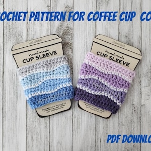 Puede incluir: Dos calentadores de taza de café de ganchillo en diferentes patrones de colores. Los calentadores están hechos con un patrón a rayas en tonos de azul y gris, y morado y rosa. Los calentadores están etiquetados como "funda de taza hecha a mano" y "HnHStitch".