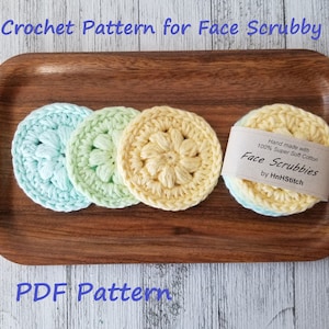 May include: Four crocheted face scrubbies in shades of blue, green, and yellow on a wooden tray. The scrubbies are made with 100% super soft cotton and are hand-made. The text "Face Scrubbies by HnHStitch" is on a label attached to the scrubbies.