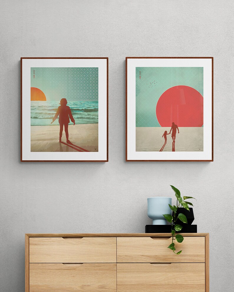 May include: Two framed prints with a beach theme. The first print shows a person standing on a beach with a large red sun setting in the distance. The second print shows two people walking on a beach with a large red sun in the sky.