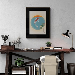 May include: A framed print of a koi fish swimming in a circle with water lilies and a Japanese character. The print is hanging on a white wall above a wooden desk with a lamp, books, and a chair.