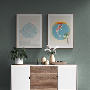 May include: Two framed prints with Japanese-inspired designs. The left print features a blue and white circle with waves and the right print features a red and white fish in a blue circle. The prints are hanging on a green wall above a white and wood cabinet with three drawers.