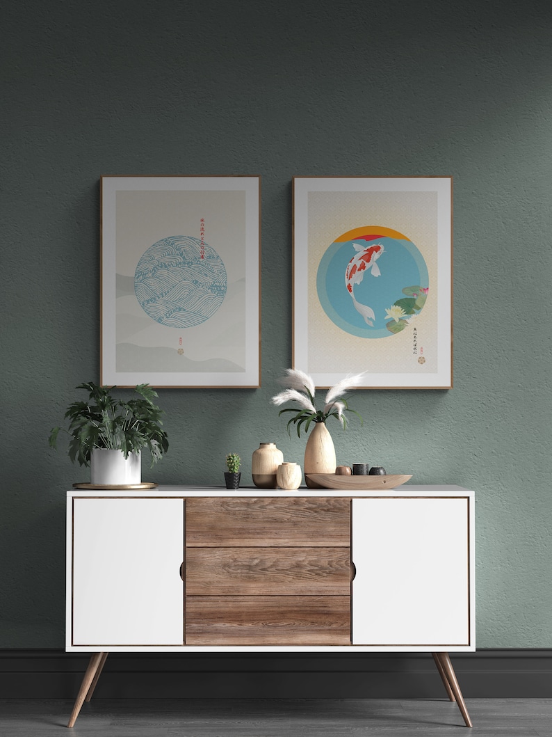 May include: Two framed prints with Japanese-inspired designs. The left print features a blue and white circle with waves and the right print features a red and white fish in a blue circle. The prints are hanging on a green wall above a white and wood cabinet with three drawers.
