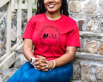 May include: A woman wearing a red t-shirt with a black circle design that says "Design Your Here M+M Your Design Here". She is sitting on stone steps with her hands in her lap.