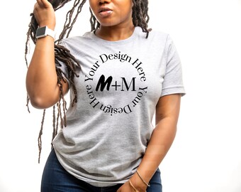 May include: A gray t-shirt with a black circle design that says "Design Your Here Your Design Here" with the letters M+M in the center.