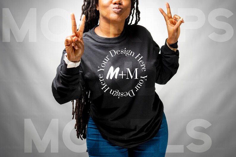 May include: A black long-sleeved shirt with a white circle design that says "Design Your Here Here Your Design M+M". The person wearing the shirt is smiling and giving a peace sign with both hands.