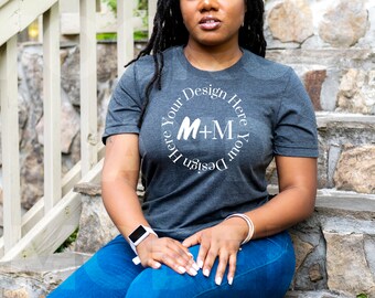 May include: A dark gray t-shirt with a white circle design featuring the text "Design Your Here M+M Your Design Here".