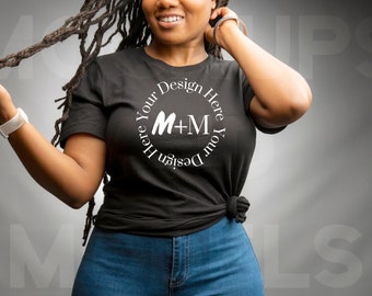 May include: A black t-shirt with a white circle design that says "Design Your Here M+M Here Your Design". The shirt is worn by a person with dreadlocks and is tied at the waist.