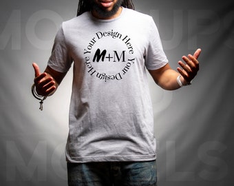 May include: A person wearing a grey t-shirt with a black circle design that says "Design Your Here M+M Your Design Here".
