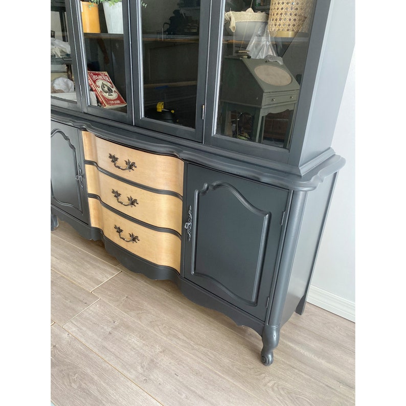 May include: A black and wood china cabinet with glass doors and three drawers. The cabinet has a curved front and ornate details.