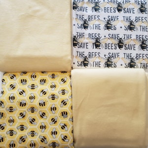 Könnte beinhalten: Vier verschiedene gelbe Stoffmuster mit Bienendesigns. Der obere linke Stoff ist einfarbig gelb mit einer subtilen Rippenstruktur. Der obere rechte Stoff hat einen weißen Hintergrund mit schwarzem Text, der "Save the Bees" lautet, und ein sich wiederholendes Muster aus gelben Bienen. Der untere linke Stoff hat einen gelben Hintergrund mit einem sich wiederholenden Muster aus schwarzen Bienen und Waben. Der untere rechte Stoff ist einfarbig gelb.