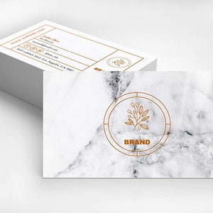 May include: A white marble business card with a gold circle containing a line drawing of a branch with leaves and the word "BRAND".