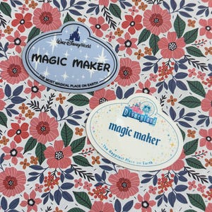 May include: Two oval-shaped name tag stickers featuring floral patterns. One light blue sticker reads Walt Disney World MAGIC MAKER THE MOST MAGICAL PLACE ON EARTH. The other white sticker reads Disneyland magic maker The Happiest Place on Earth.