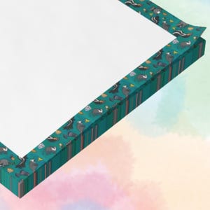 Peut inclure: Un bloc-notes blanc avec une bordure turquoise ornée d'un motif répété de moufettes, de champignons et d'autres éléments forestiers. La bordure présente des rayures verticales dans les tons de turquoise, de marron et d'orange.