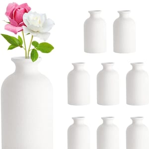 May include: Set of nine white ceramic vases, with a textured finish. The vases are arranged in three rows of three. The vases are all the same size and shape, and they are all empty.