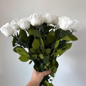 May include: A bouquet of white silk roses with green leaves.