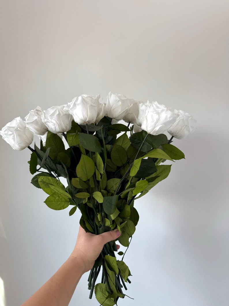 May include: A bouquet of white silk roses with green leaves.
