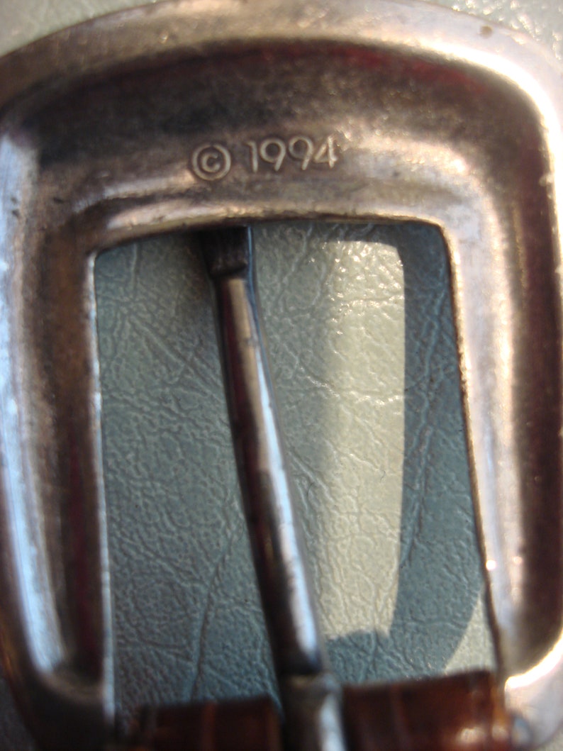May include: Close-up of a silver metal belt buckle with the inscription "&copy; 1994".