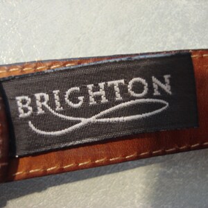 May include: A brown leather belt with a black label that reads "BRIGHTON" in white lettering. The label has a white, curved line design.