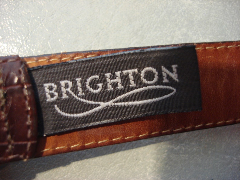 May include: A brown leather belt with a black label that reads "BRIGHTON" in white lettering. The label has a white, curved line design.