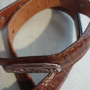 May include: A brown leather belt with a silver buckle. The buckle has a decorative design.
