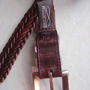 May include: A brown leather braided belt with a silver buckle and a label that reads "BRIGHTON" and "CHINA".