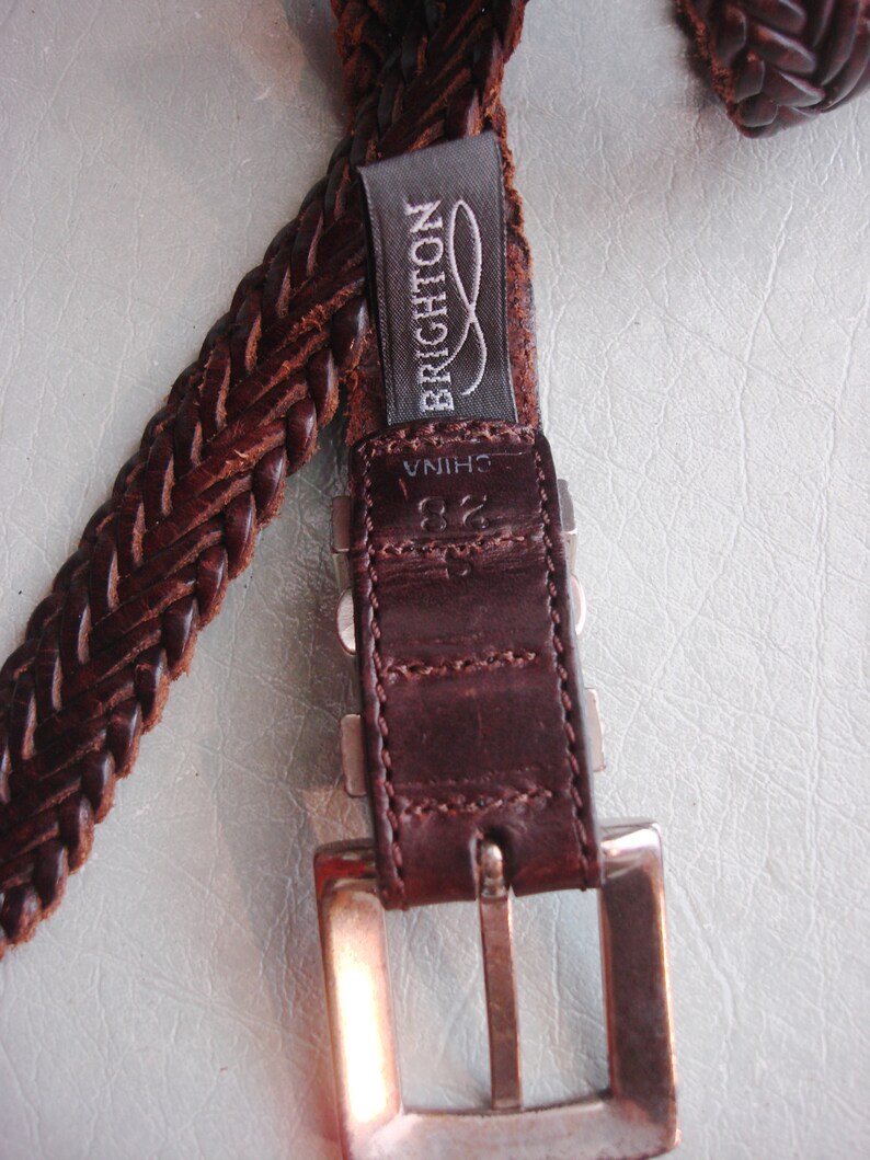 May include: A brown leather braided belt with a silver buckle and a label that reads "BRIGHTON" and "CHINA".