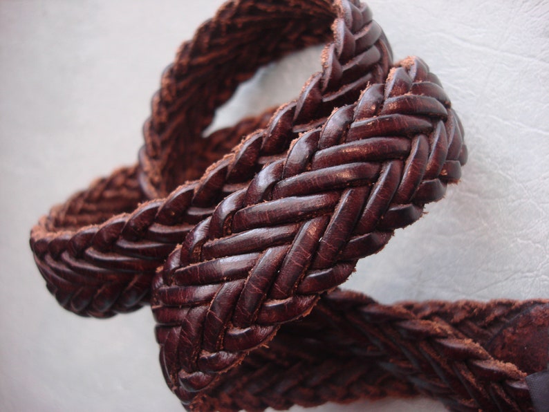 May include: A close-up of a brown leather belt with a braided design.