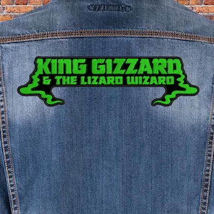 Pode incluir: Uma jaqueta de ganga azul com um remendo bordado verde e preto que diz "King Gizzard & The Lizard Wizard".