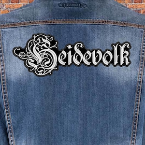 May include: A black and white embroidered patch with the word "Seidevolk" in a gothic font. The patch is sewn onto a blue denim jacket.