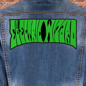 May include: A denim jacket with a large, green patch featuring the text "ELECTRIC WIZARD" in a stylized, black font. The patch is rectangular with a curved top and bottom. The jacket is a medium wash denim.