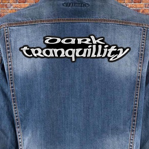 Op de afbeelding: Een blauwe denim jas met een witte en zwarte geborduurde patch met de tekst "dark tranquility" op de rug.