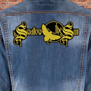 Könnte beinhalten: Ein gestickter schwarzer und gelber Aufnäher mit dem Text "Swallow the Sun" und einer Silhouette eines Nachtfalters. Der Aufnäher ist auf eine blaue Jeansjacke genäht.