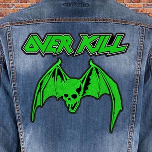 May include: A denim jacket with a green and black embroidered patch of a bat with a skull and the text "OVER KILL" in white and gray.