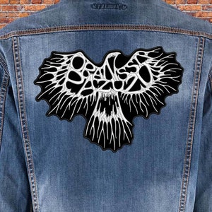 Puede incluir: Un parche bordado en blanco y negro de un águila estilizada con la palabra "BRANSO" escrita dentro de las alas.