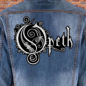 May include: A blue denim jacket featuring a large, embroidered patch on the back. The patch is black with a white, intricate, swirling design and the text Opeth in a stylized, gothic-inspired font, centered on the back panel of the jacket.