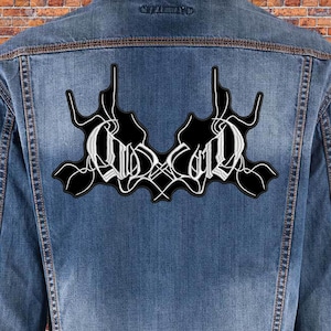 Può includere: Una giacca di jeans nera con una toppa ricamata bianca sul retro che dice "GOD" in un font gotico.