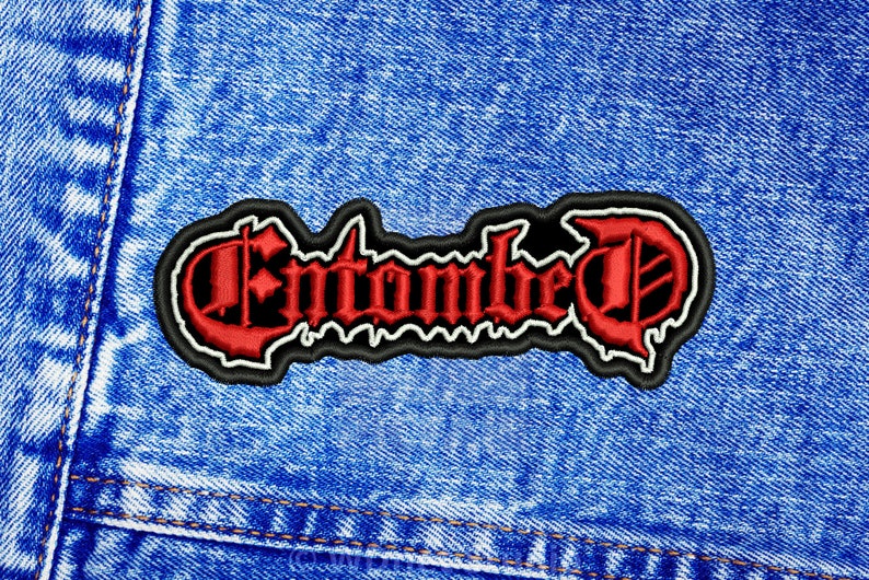 K&ouml;nnte beinhalten: Ein roter und wei&szlig;er gestickter Aufn&auml;her mit dem Wort "Entombed" in gotischer Schrift auf einem blauen Jeansstoff.
