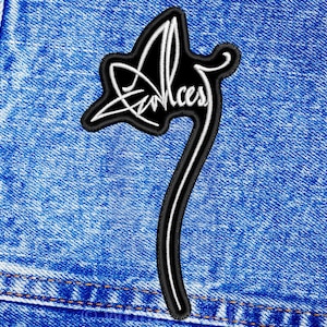 May include: Black and white embroidered patch with the word "Envy" in a stylised font. The patch is sewn onto a blue denim background.