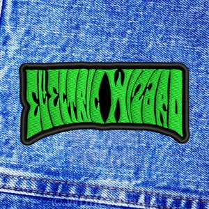 May include: A green embroidered patch with the text "STRANGE WORLD" in a wavy, psychedelic font. The patch has a black border and is set against a blue denim background.