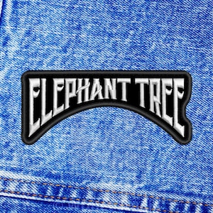 Op de afbeelding: Een geborduurde zwarte en witte patch met de tekst "Elephant Tree" in een gebogen boog. De patch is genaaid op een blauwe denim stof.