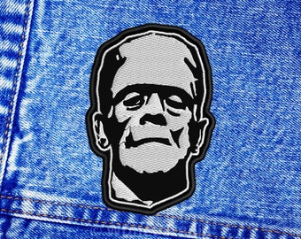 Può includere: Toppa ricamata in bianco e nero del volto di Frankenstein su uno sfondo di denim blu.