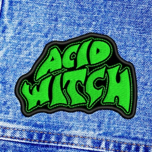 May include: Green and black embroidered patch with the text "Acid Witch" on a blue denim background.