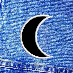 May include: A crescent moon shape cut out of a blue denim fabric. The moon is outlined in white.