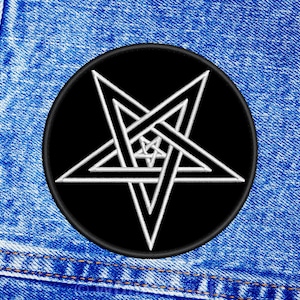 Può includere: Una toppa pentagramma nera e bianca con un contorno bianco su un cerchio nero. La toppa è cucita su un tessuto di jeans blu.