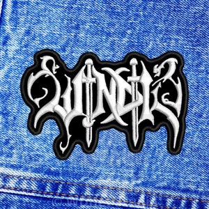 Może przedstawiać: Biała haftowana naszywka z napisem "WÜNDER" w stylu gotyckim na czarnym tle. Naszywka jest przyszyta do niebieskiej dżinsowej kurtki.