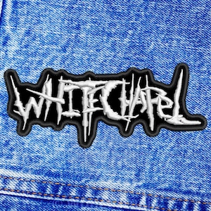 以下が含まれることがあります： 青いデニムの背景に、ホワイトチャペルバンドのロゴが刺繍されたパッチ