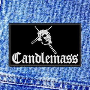 May include: Black and white embroidered patch featuring a skull and crossbones design with the text "Candlemass".
