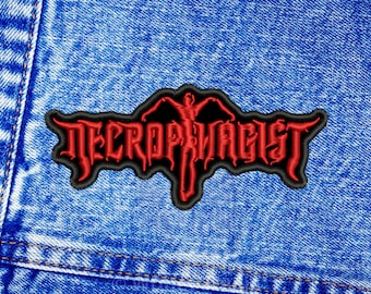 May include: Red embroidered patch with the text "NECROPHAGIST" in a black gothic font. A red figure with outstretched arms is in the centre of the patch.
